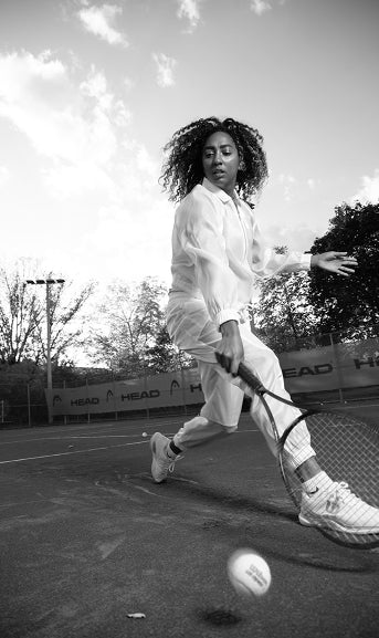 Person playing tennis on a court with trees and sky in the background